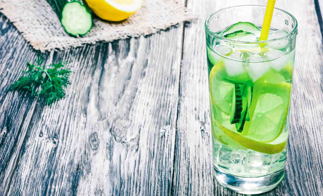 Glass of Green Dream on a wooden table with cucumber and lemon on a mat