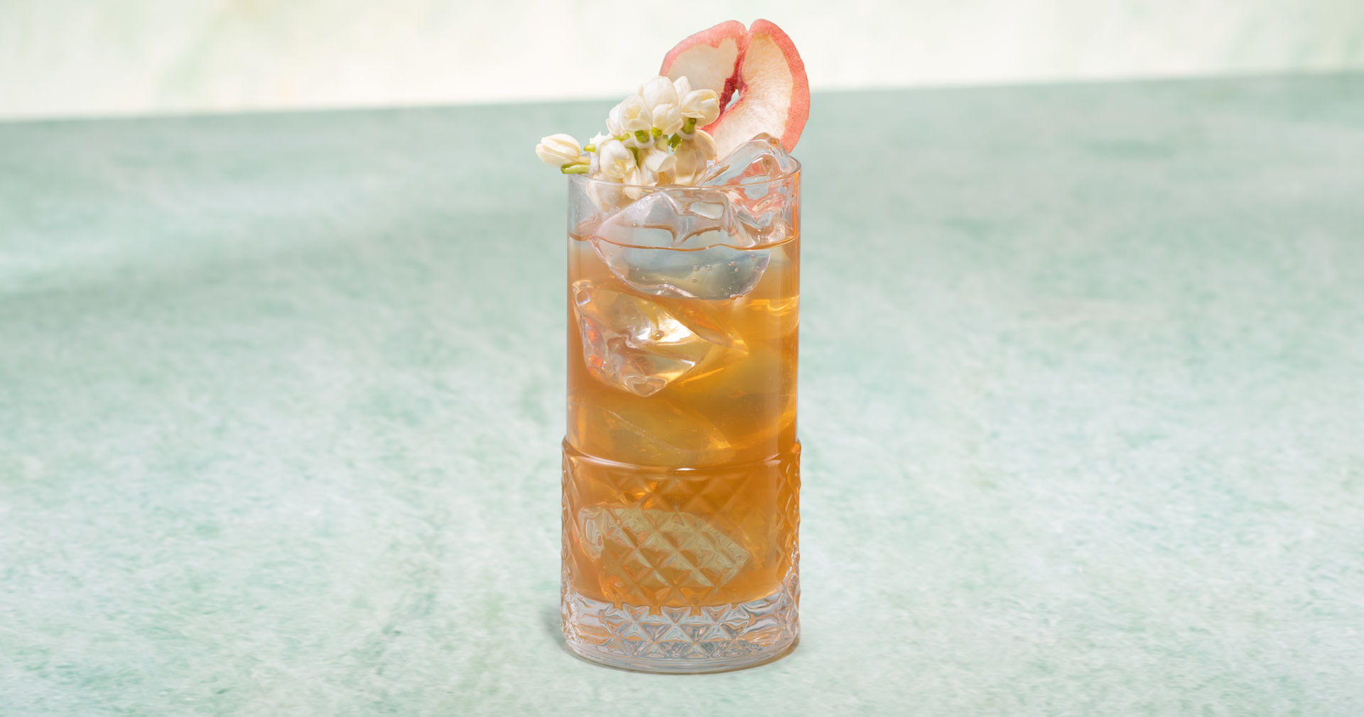 Glass of Peach & Jasmine Iced Tea on a green stone surface