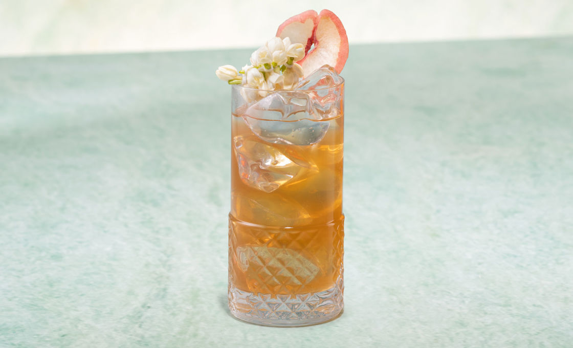 Glass of Peach & Jasmine Iced Tea on a green stone surface