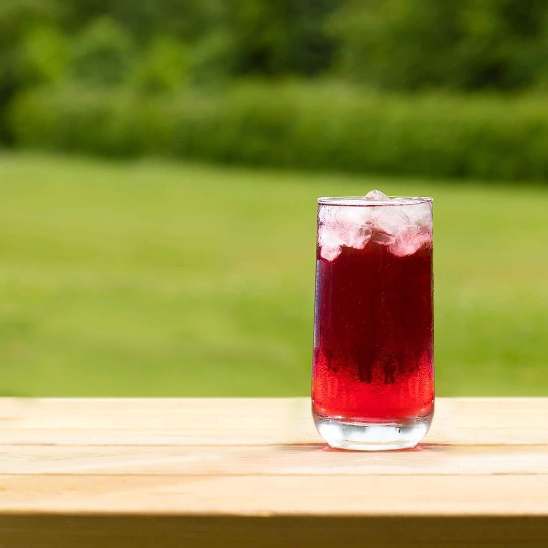 Glass of Fruity Delite on a wooden table with a grassy field in the background
