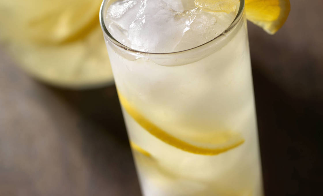A jug and glass of lemonade with sliced lemons on a wooden table