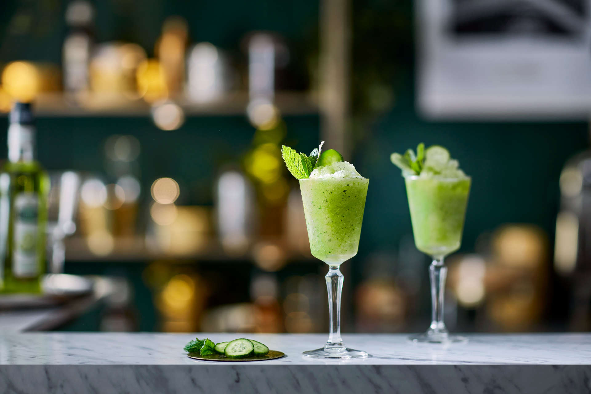 Two glasses of Sunshine Slushie on a bar with cucumber slices