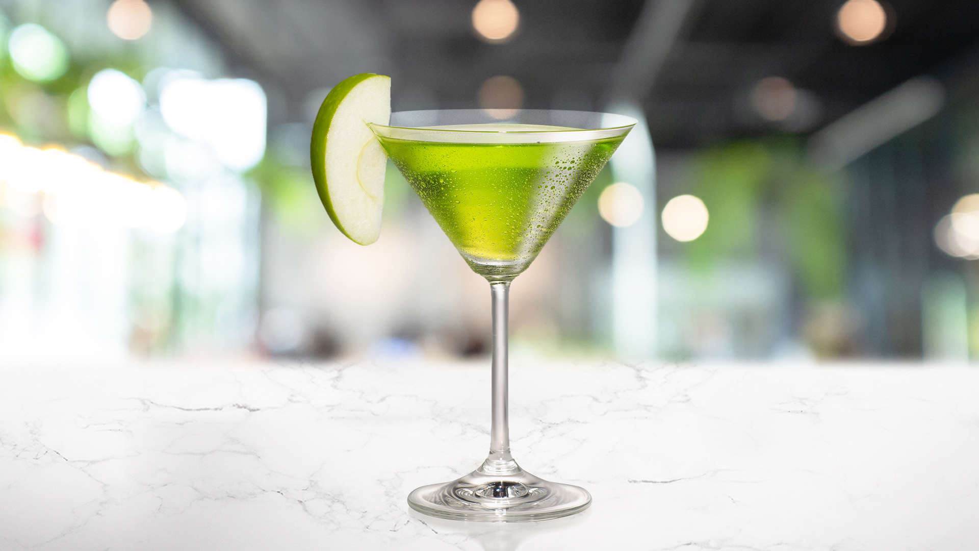 A glass of Appletini with a sliced apple on a white background