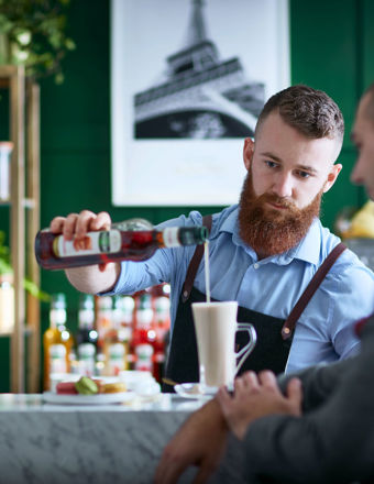 Bearded man pours syrup into a glass for a customer
