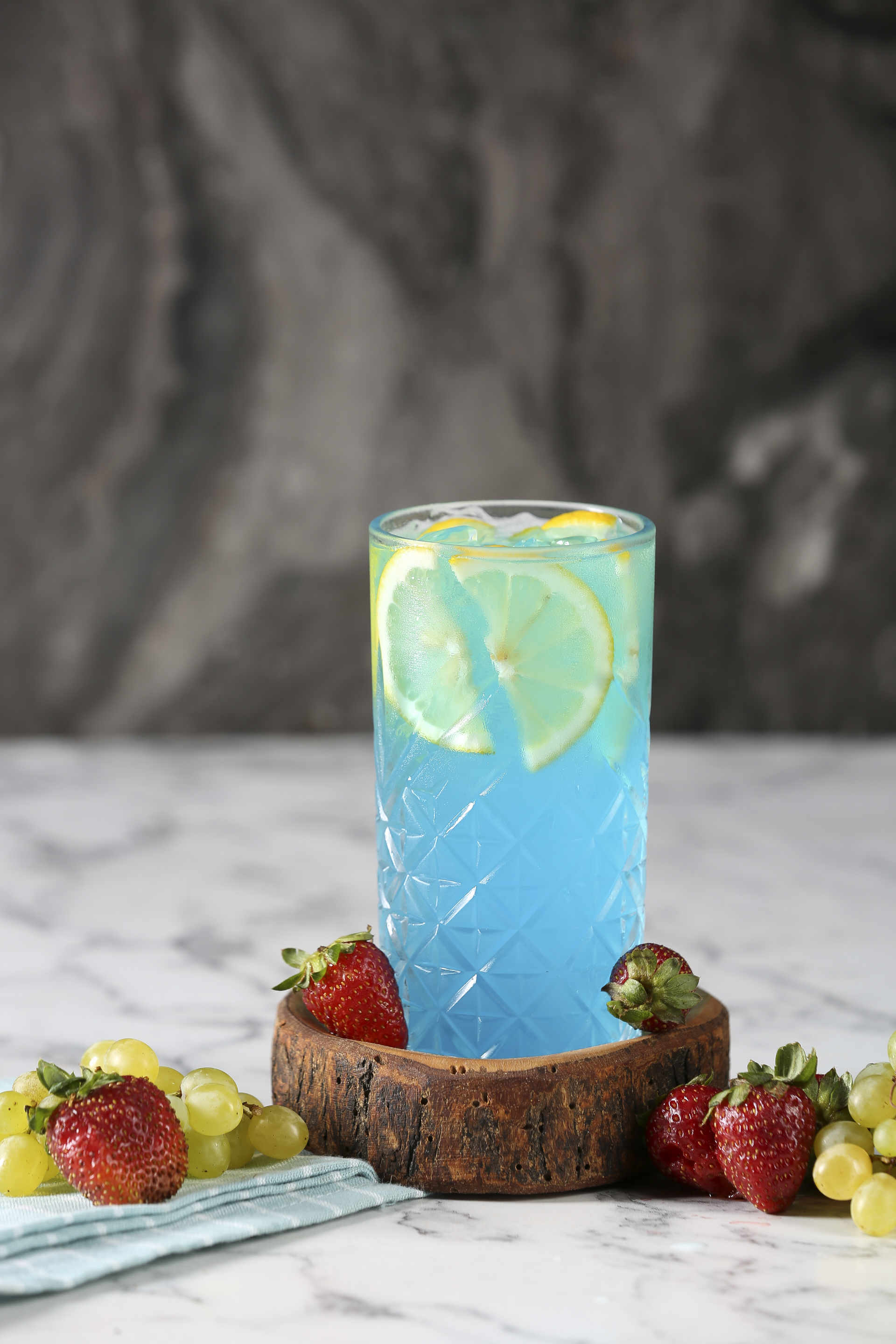 Glass of Blu Tonic in a crude wooden tray with strawberries and grapes