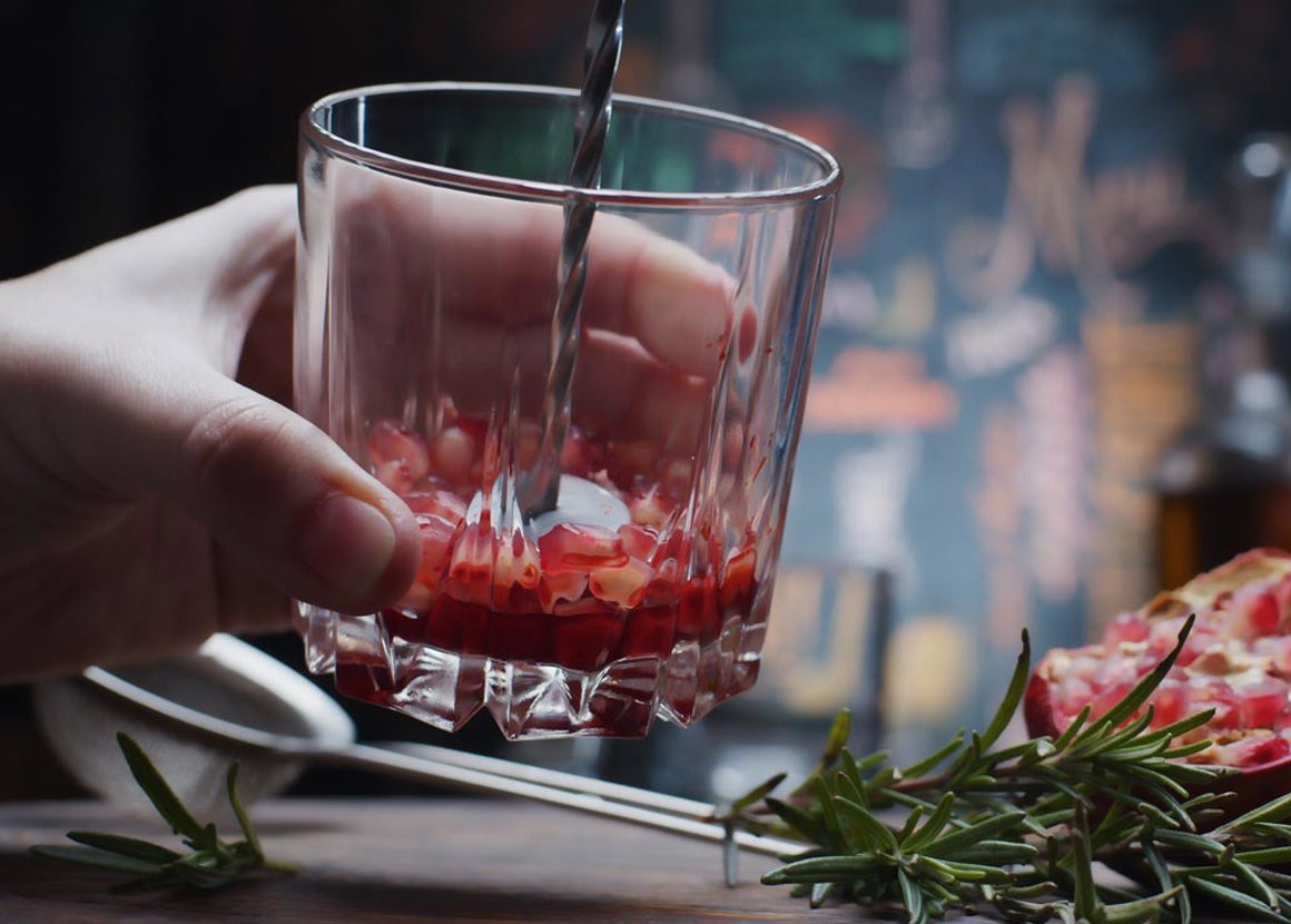 A glass containing fruit at the bottom is being muddled, and the rest of the fruit sits on the bar.