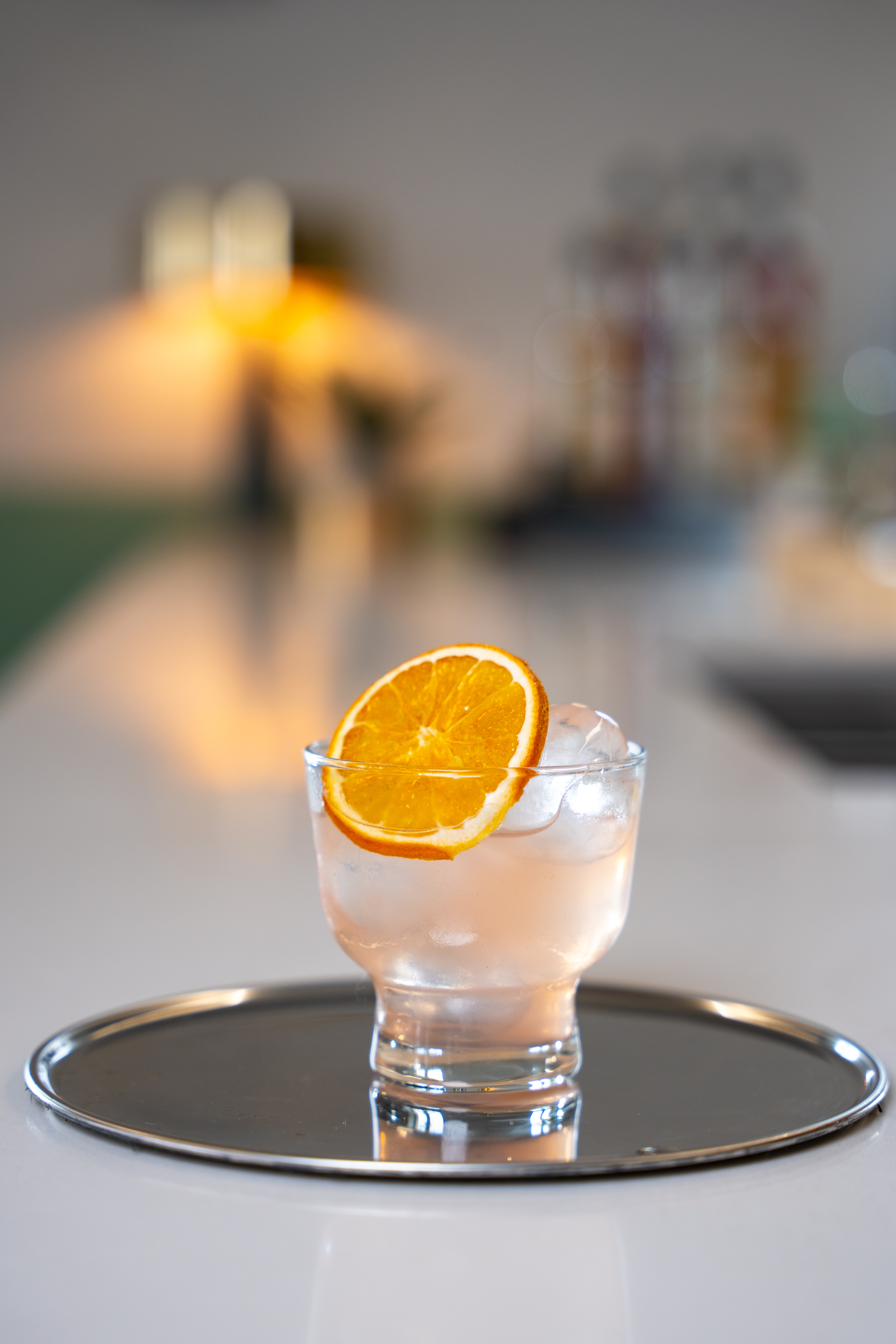 A small glass is placed on a silver tray. The drink is topped with a slice of fresh grapefruit. 