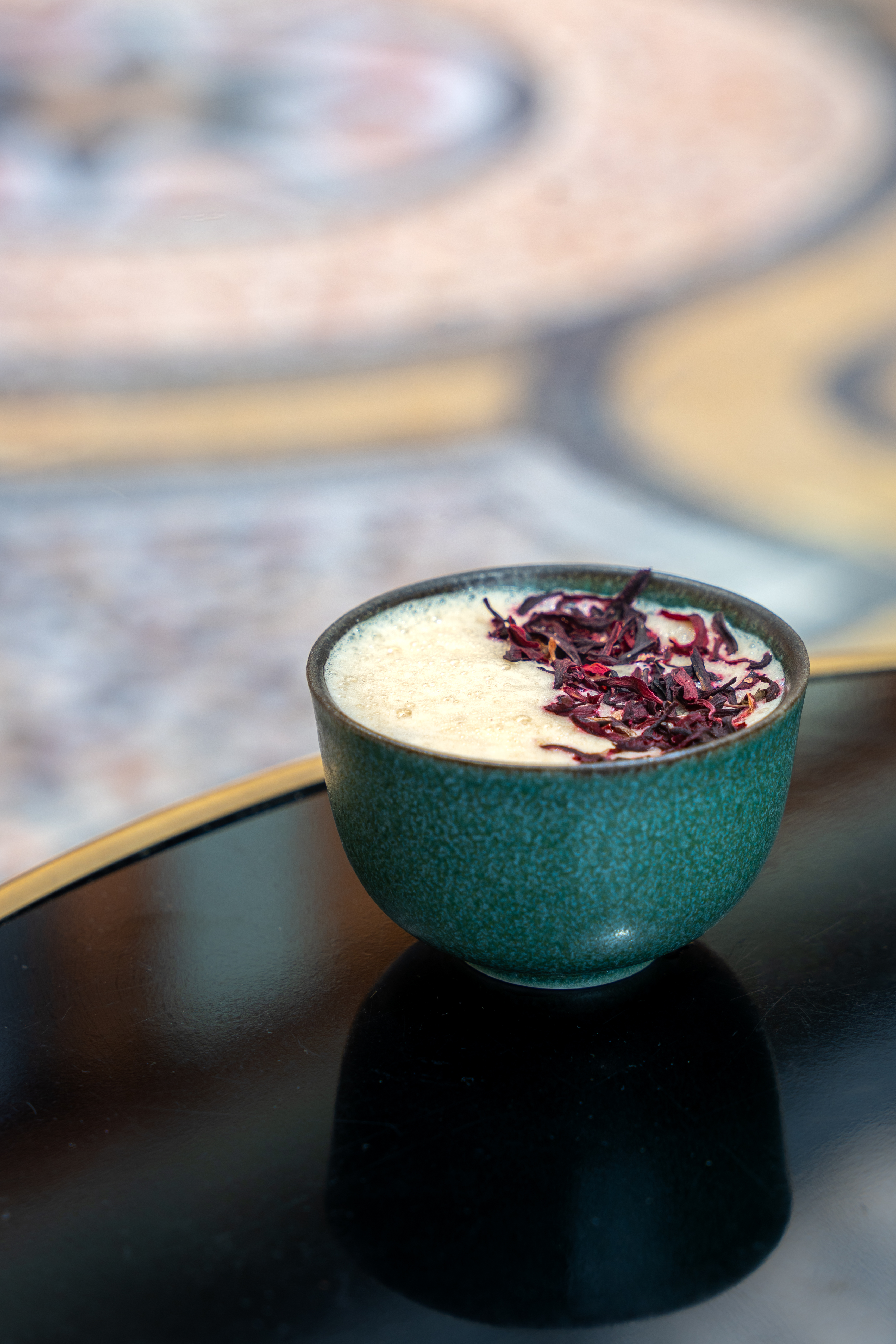 On the edge of a black coffee table there is a small coffee mug. In the mug there is a frothy coffee. 