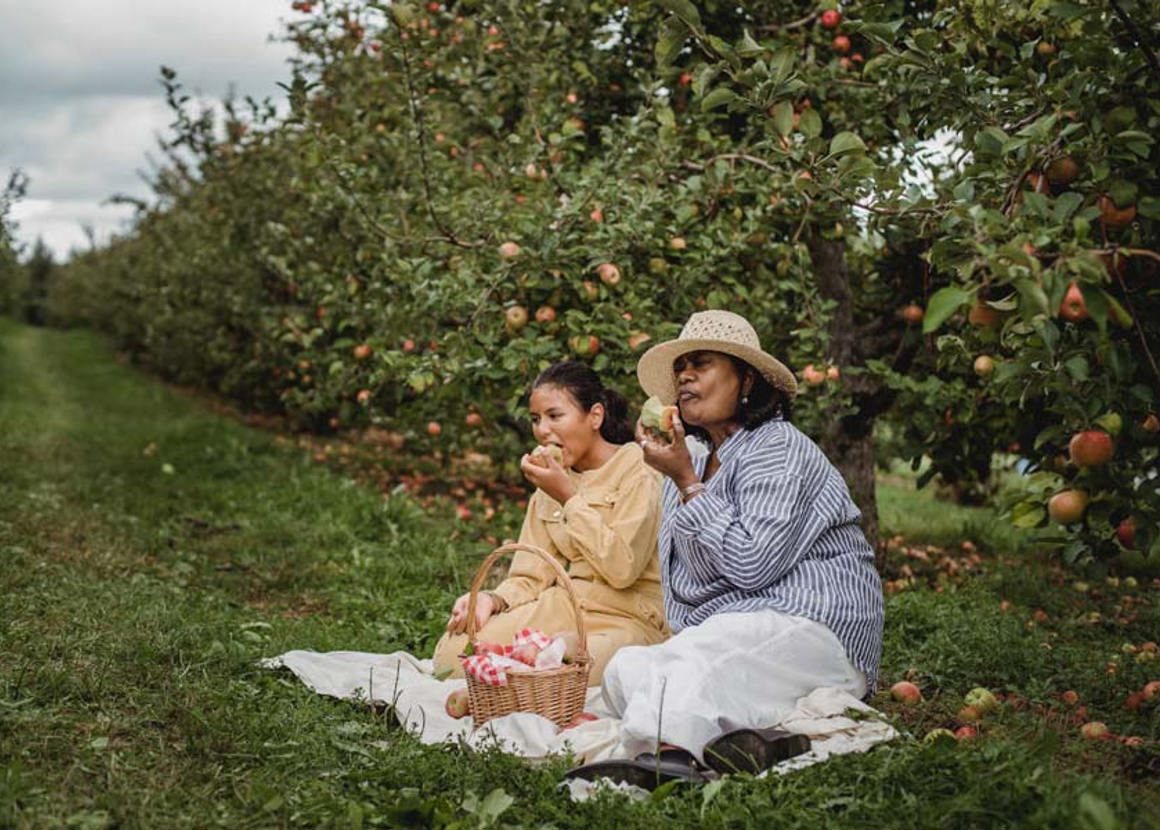 Two women sitting in an orchard eating fruit