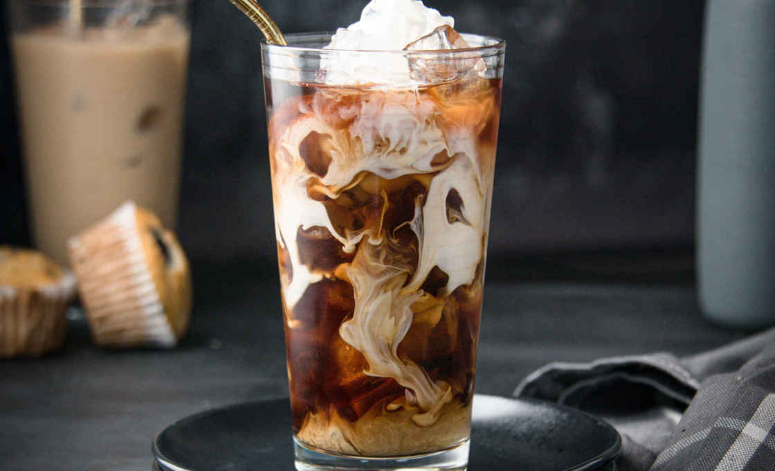 A Chestnut Iced Latte in a highball glass with milk being poured on top