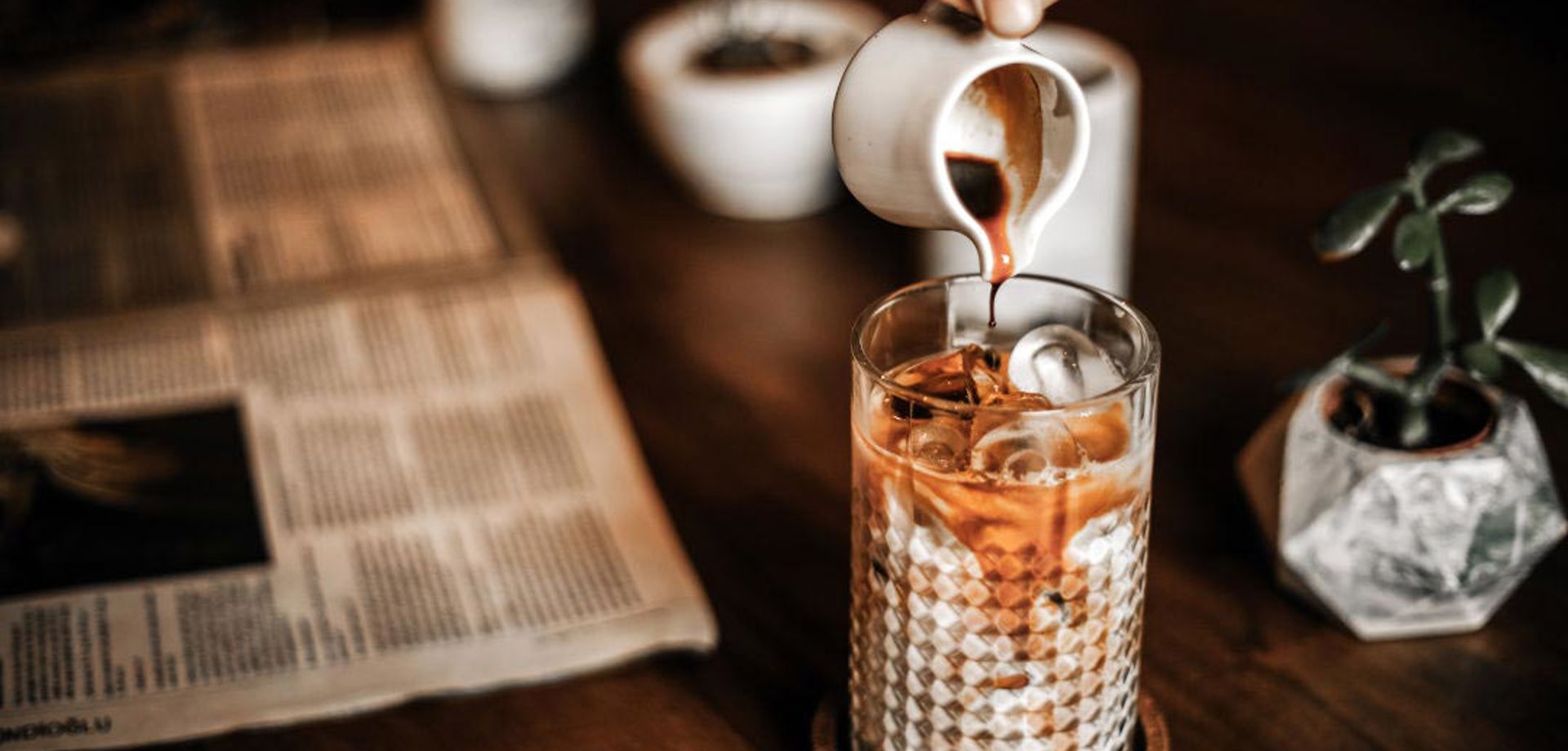 coffee being poured into a glass with a newspaper and small potted plants