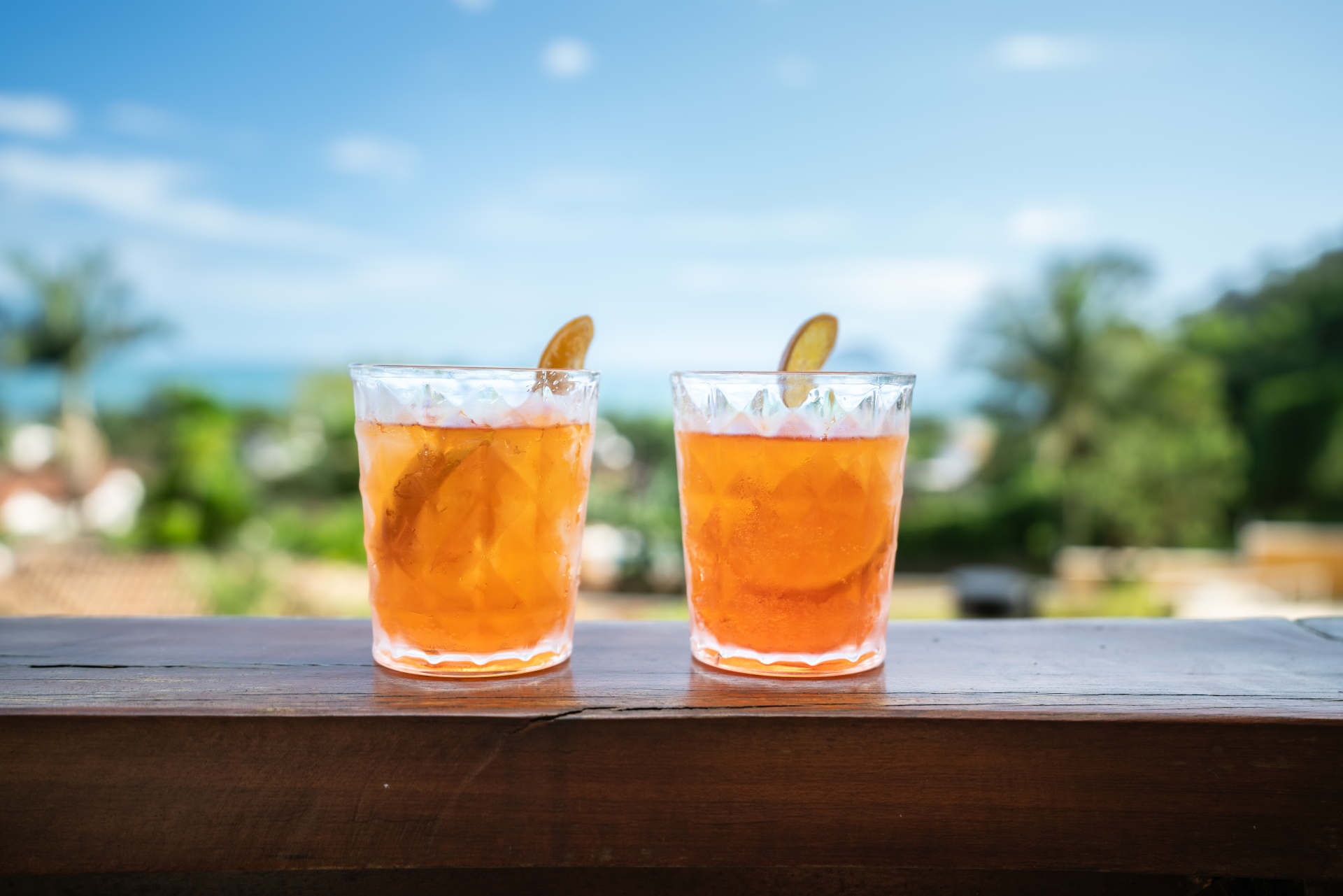 two glasses of Orange Spritz Radler on a wooden surface with a tropical background