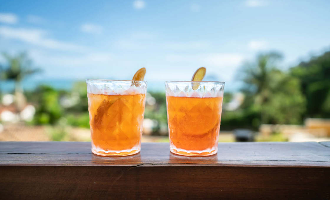 two glasses of Orange Spritz Radler on a wooden surface with a tropical background