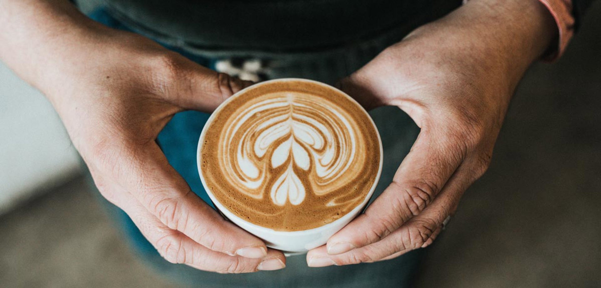 A barista is holding a coffee cup, filled with a coffee topped with decorative latte art.