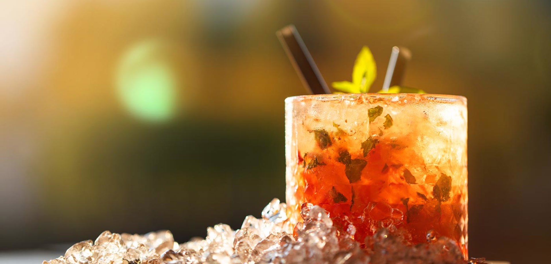 A short cocktail glass filled with crushed ice and greens sits on a wooden board.