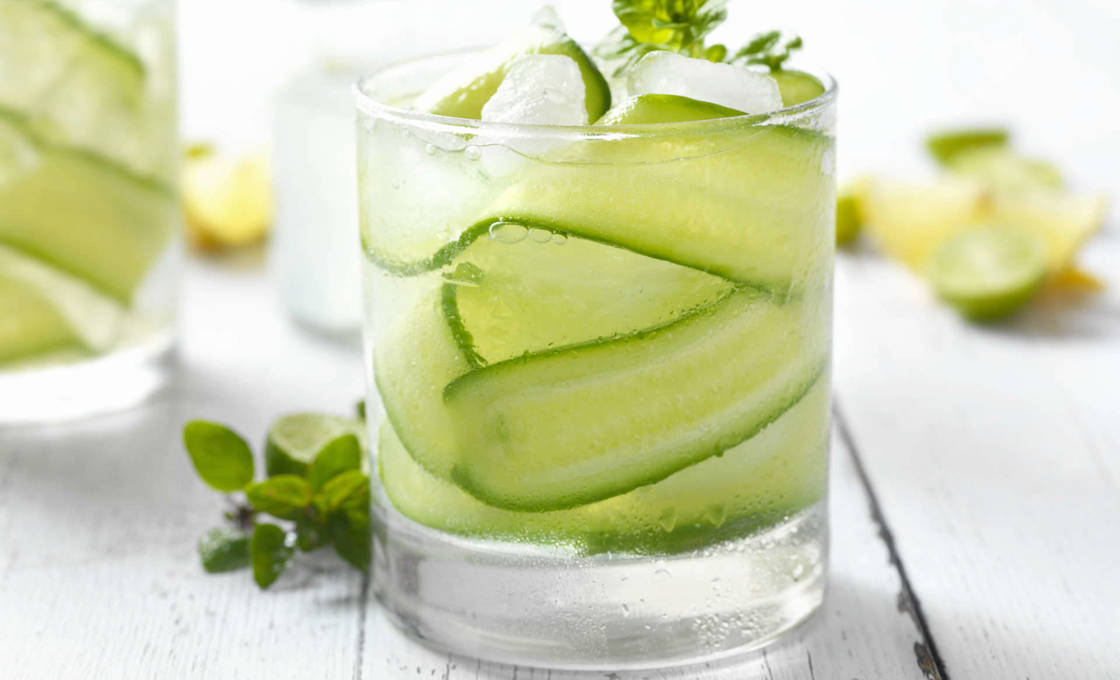 A glass of cucumber and basil soda on a white wooden table