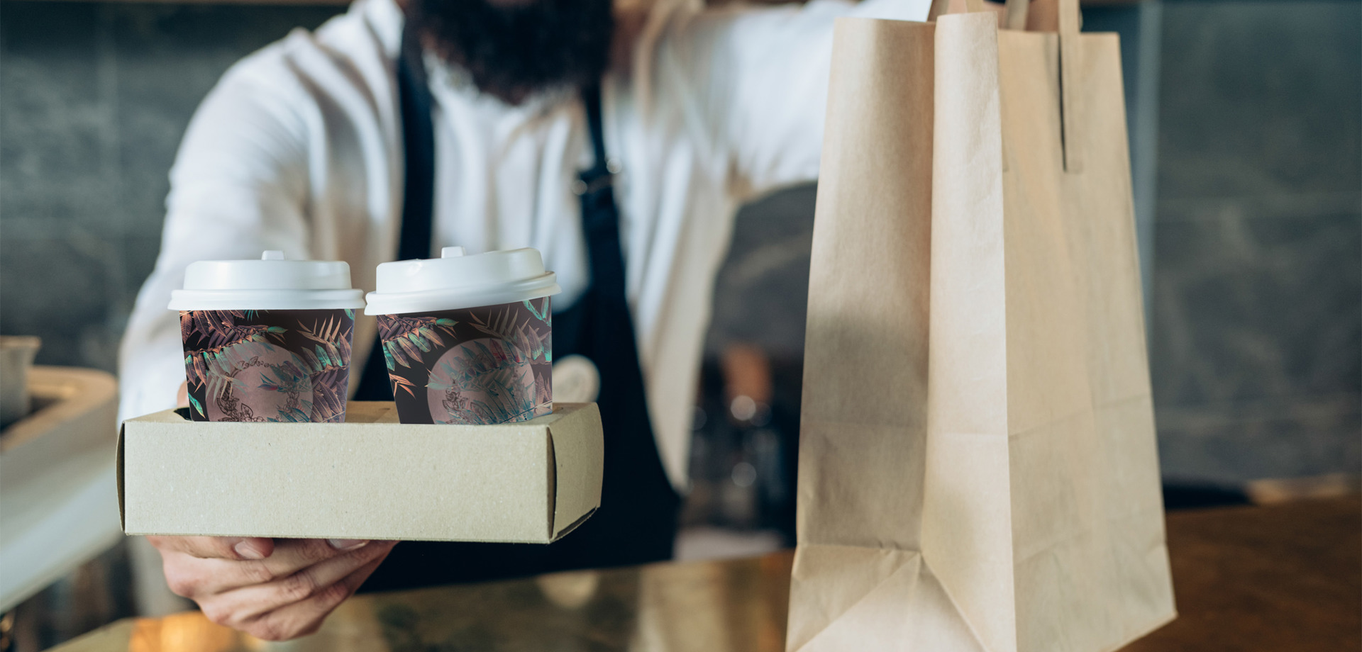 A barista handing over two cups of coffee and brown bag 