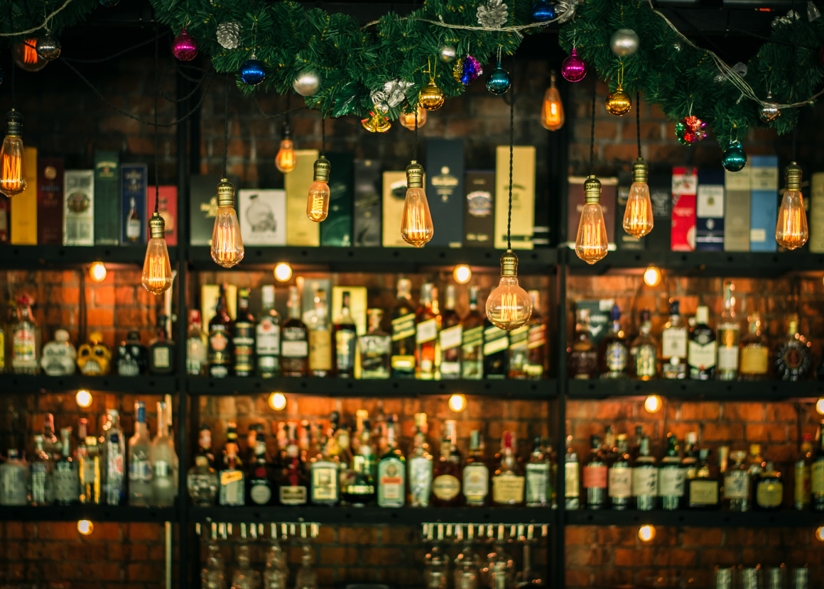 A bar is lined with christmas lights and decorations. In the background we can see bottles of spirits. 