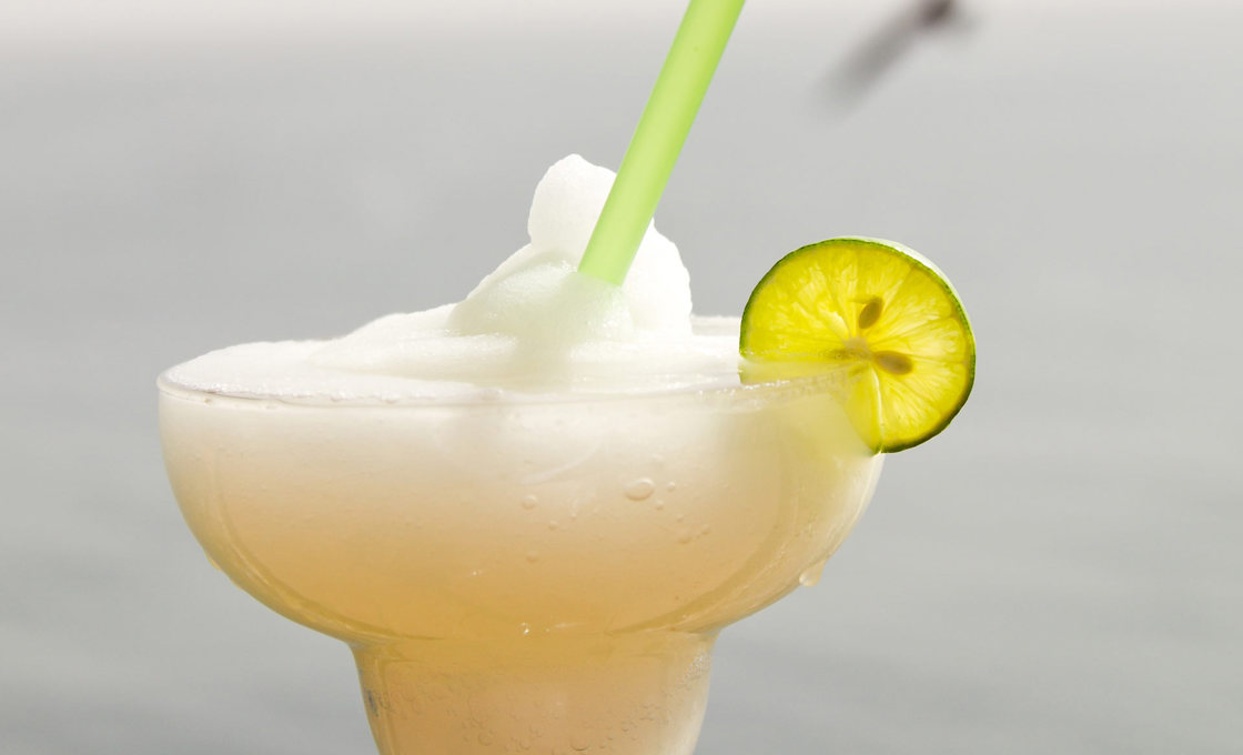 A bartender placing a sliced lime on a banana margarita cocktail