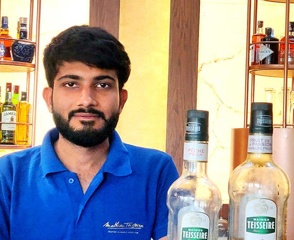 Brijesh Yadav behind a bar with two bottles of Mathieu Teisseire syrup 